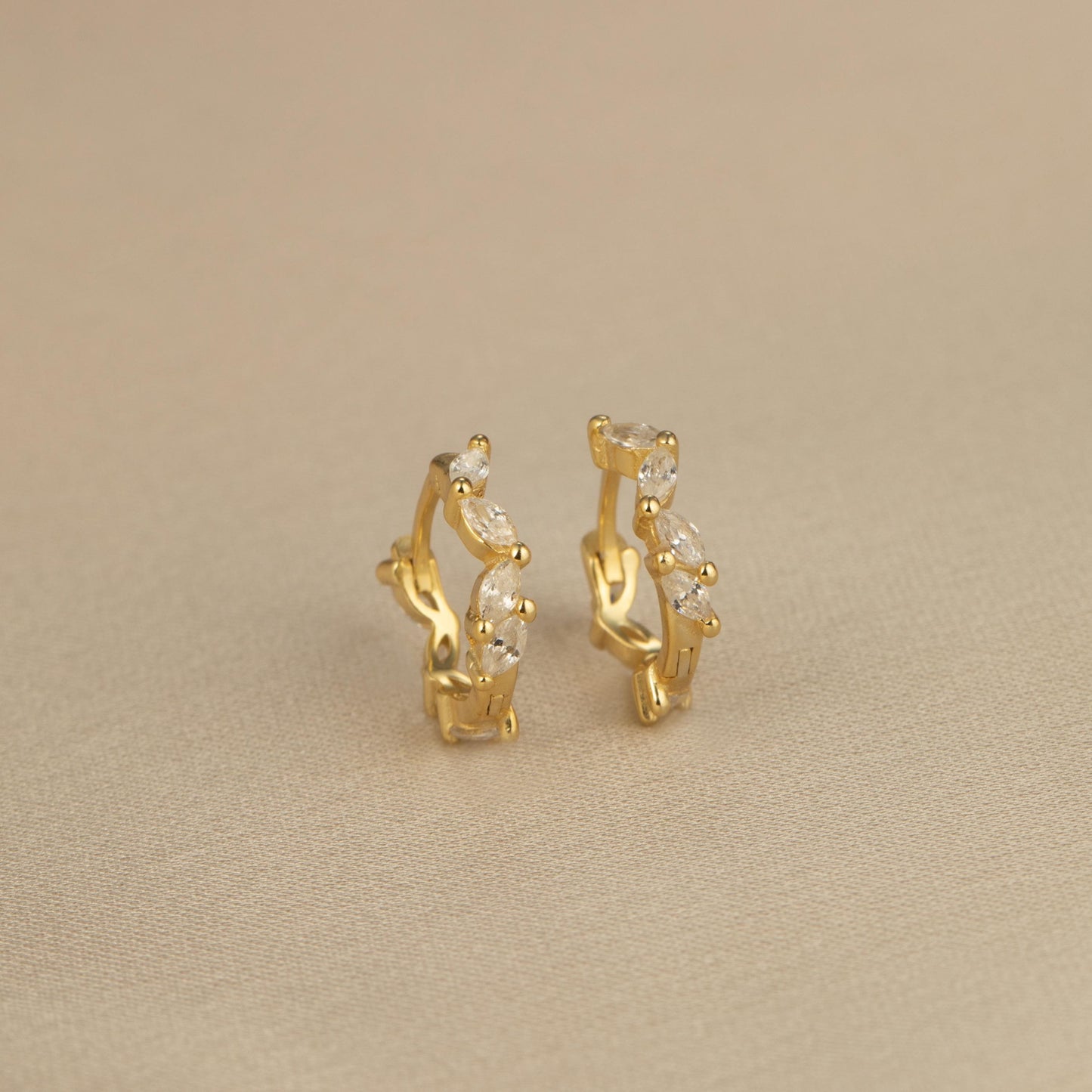 a pair of gold earrings on a beige surface