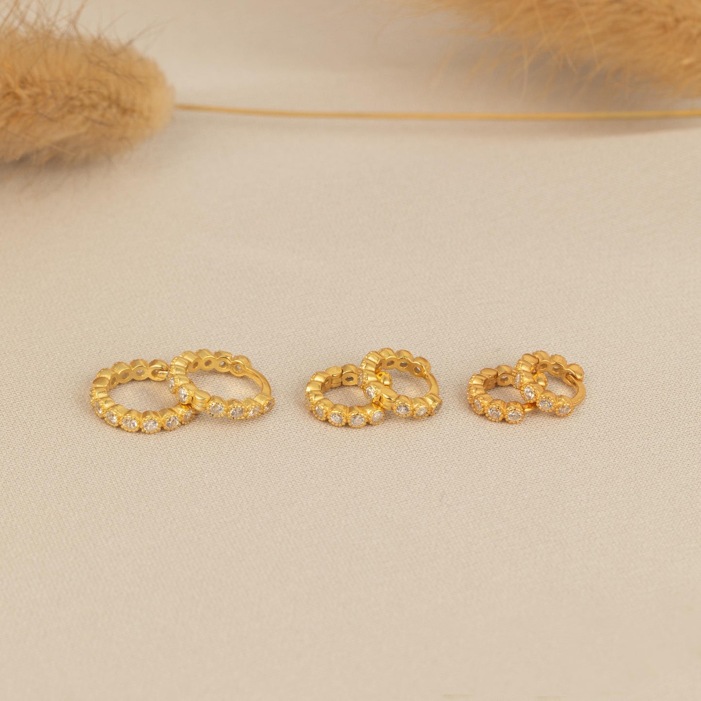 three pairs of gold earrings on a white surface