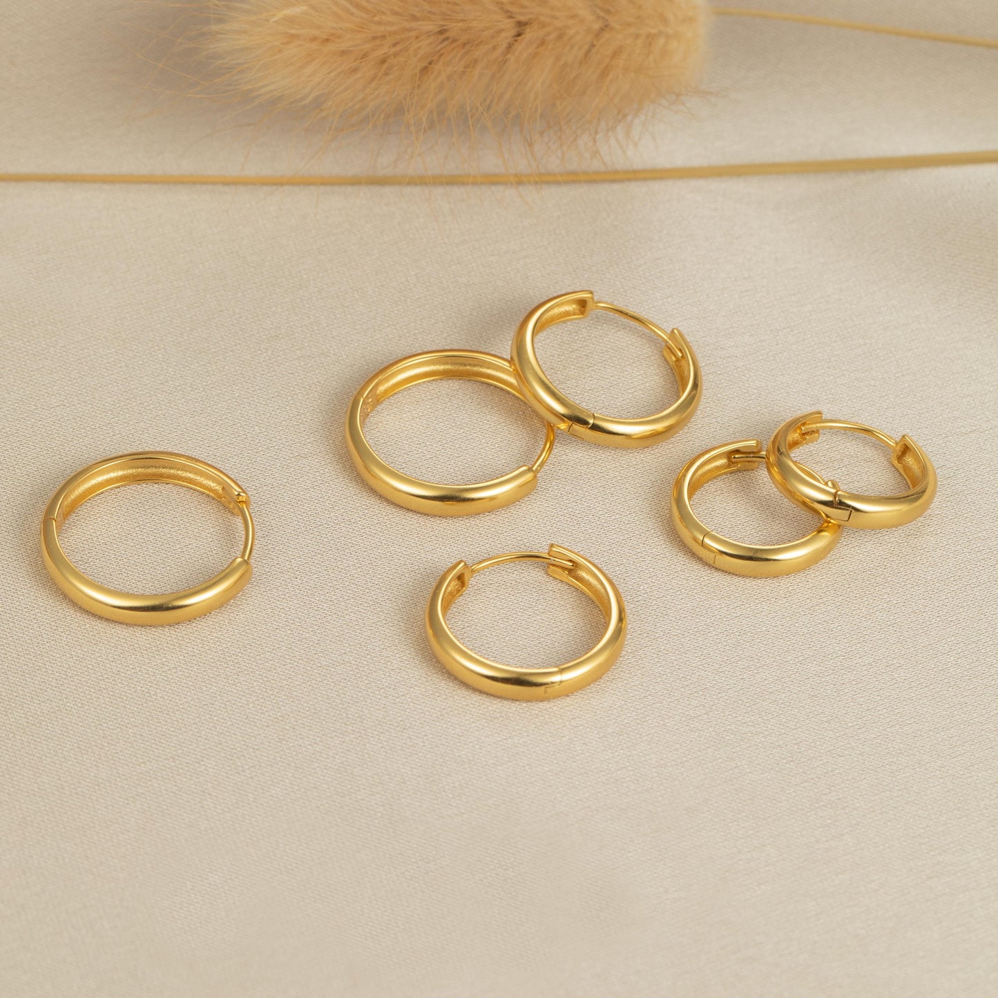 five pairs of gold hoop earrings on a white surface