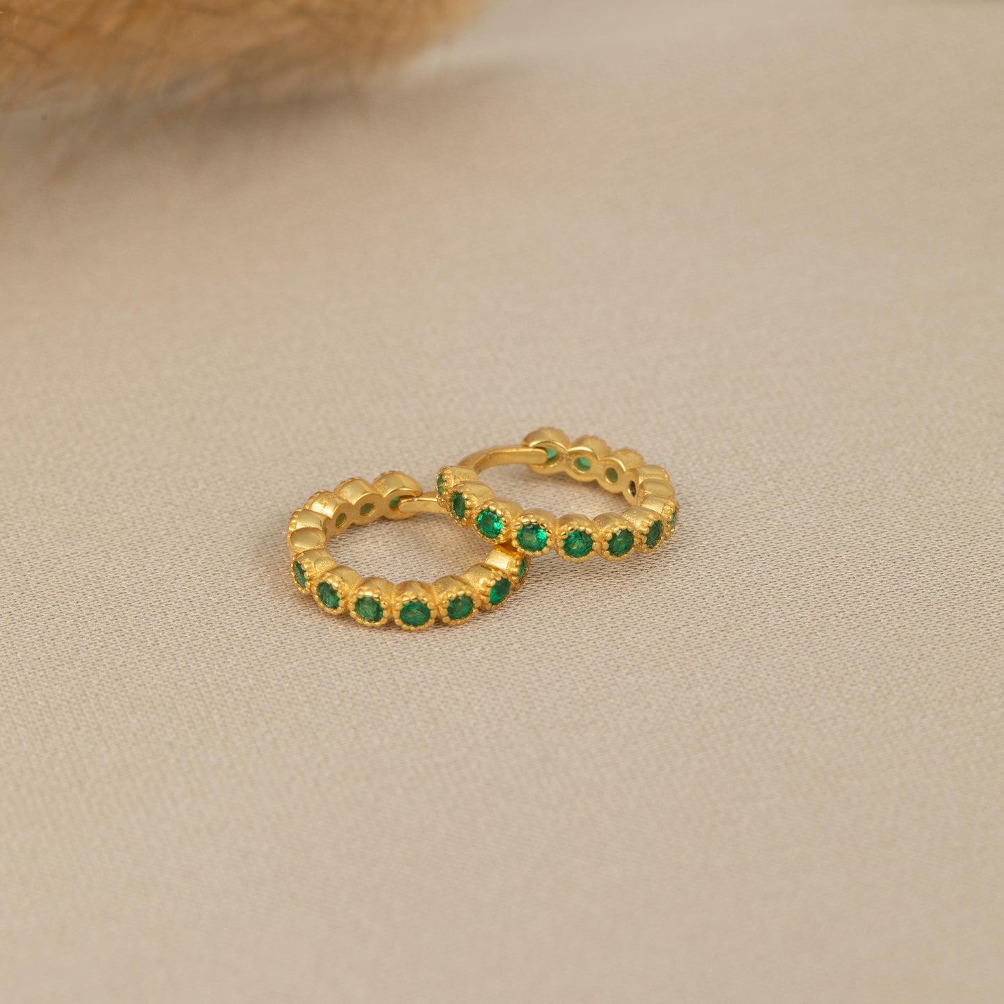 a pair of gold hoop earrings with emerald stones