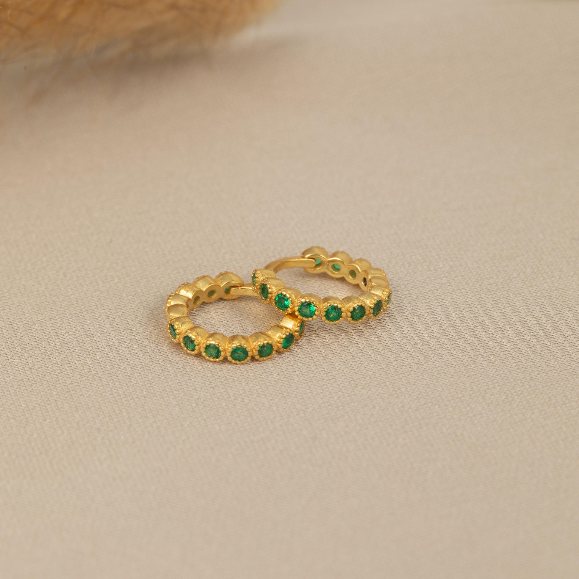 a pair of gold hoop earrings with emerald stones