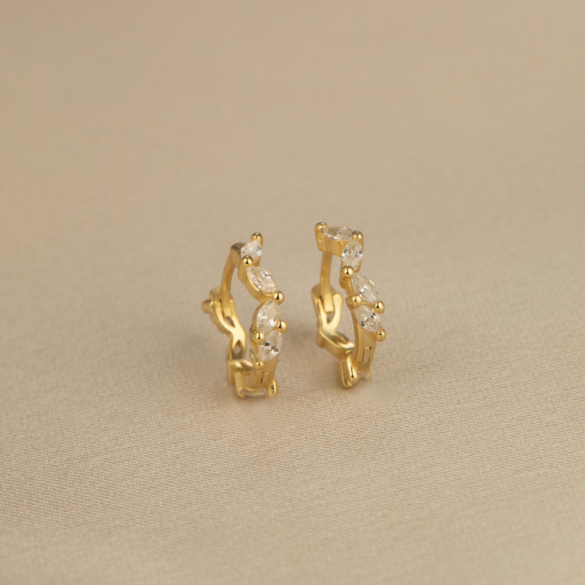 a pair of gold earrings on a beige surface
