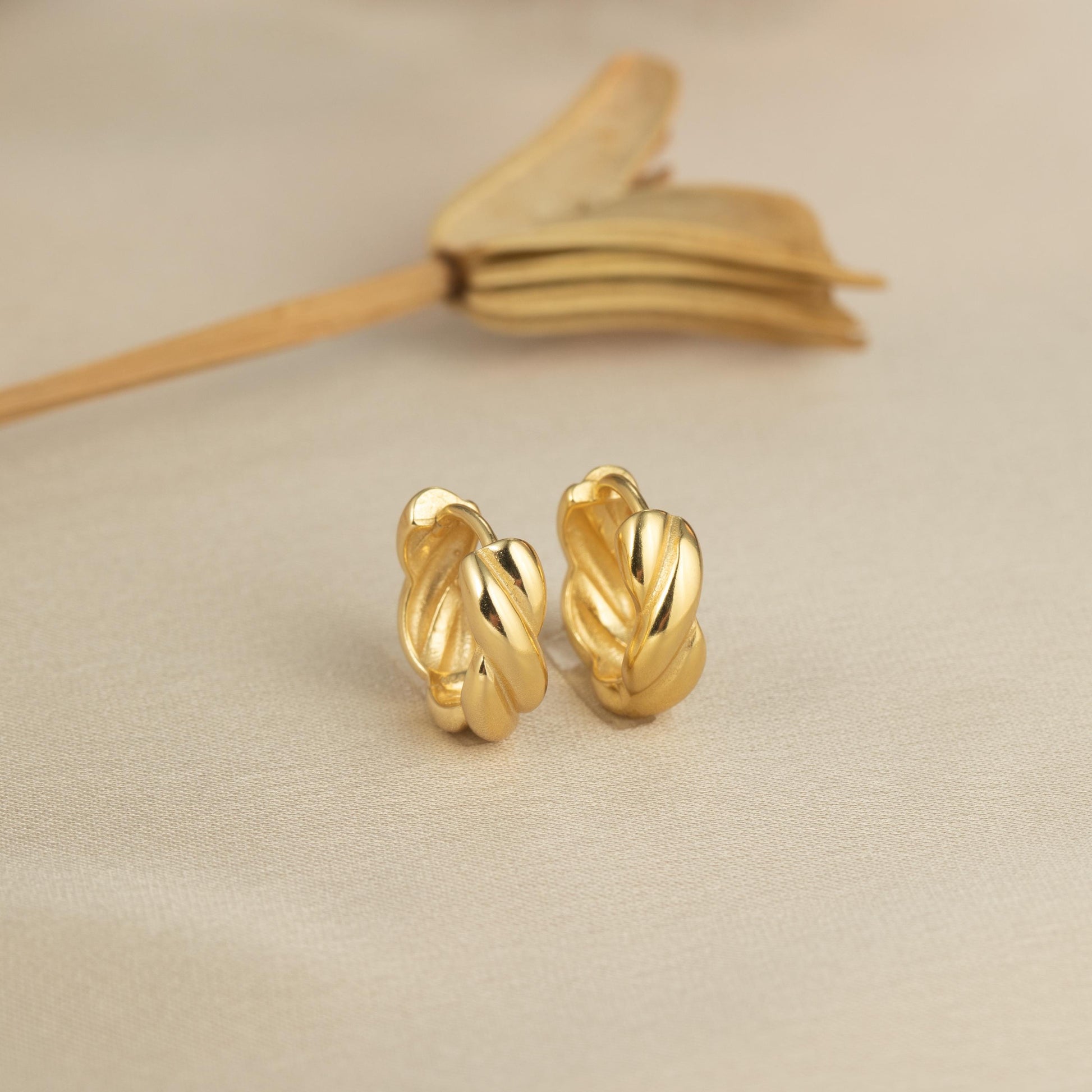 a pair of gold earrings sitting on top of a table
