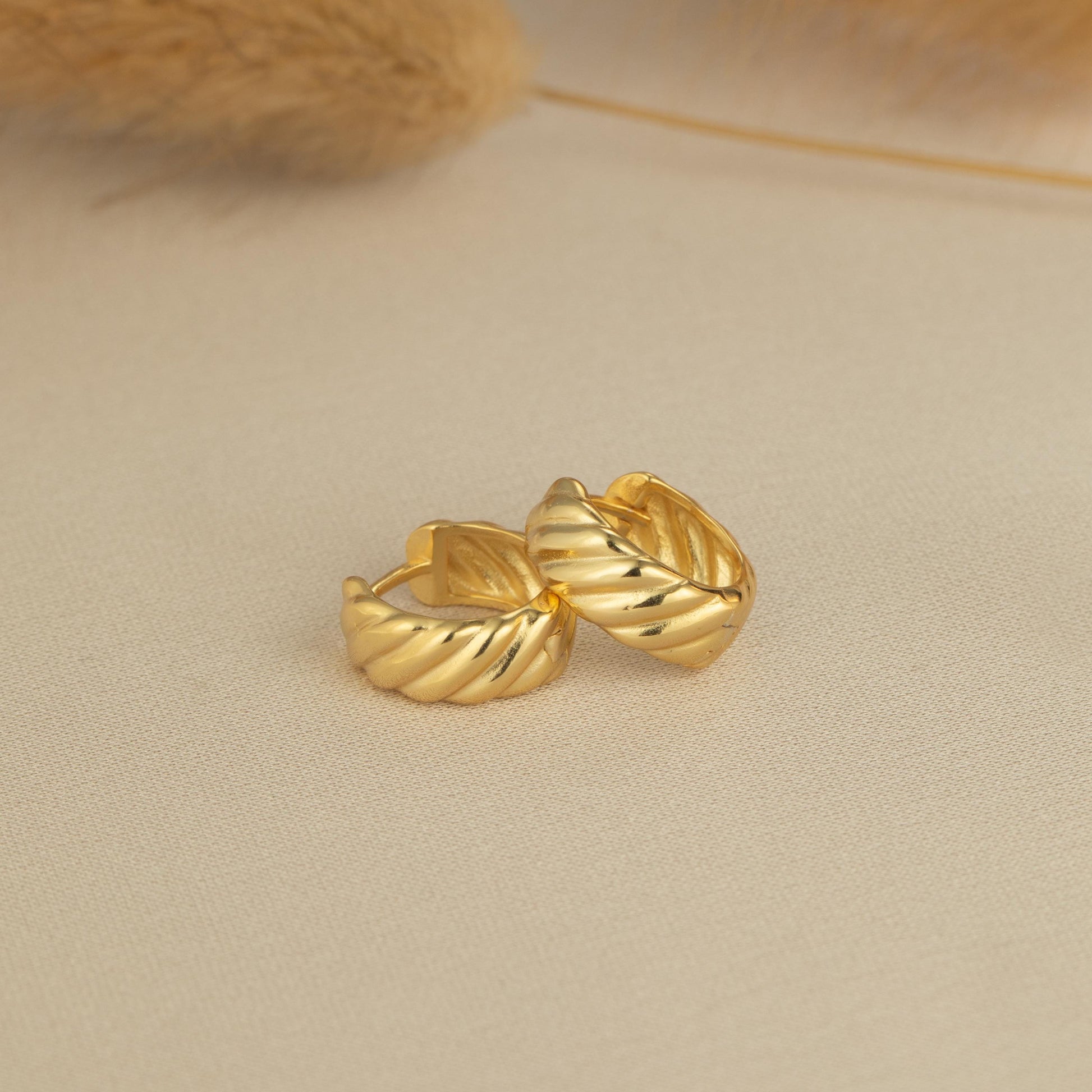 a pair of gold earrings sitting on top of a white surface