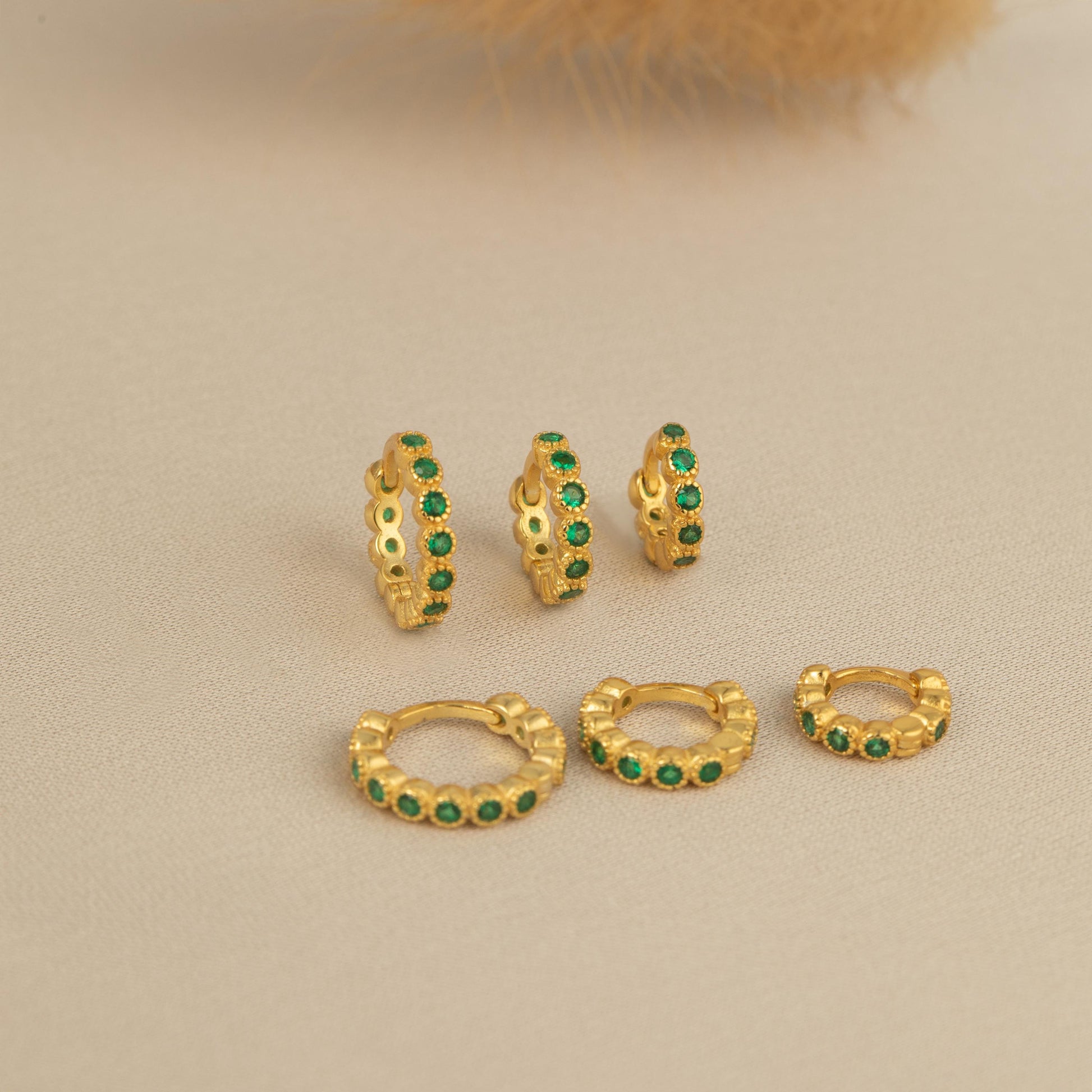 three pairs of gold earrings with green stones