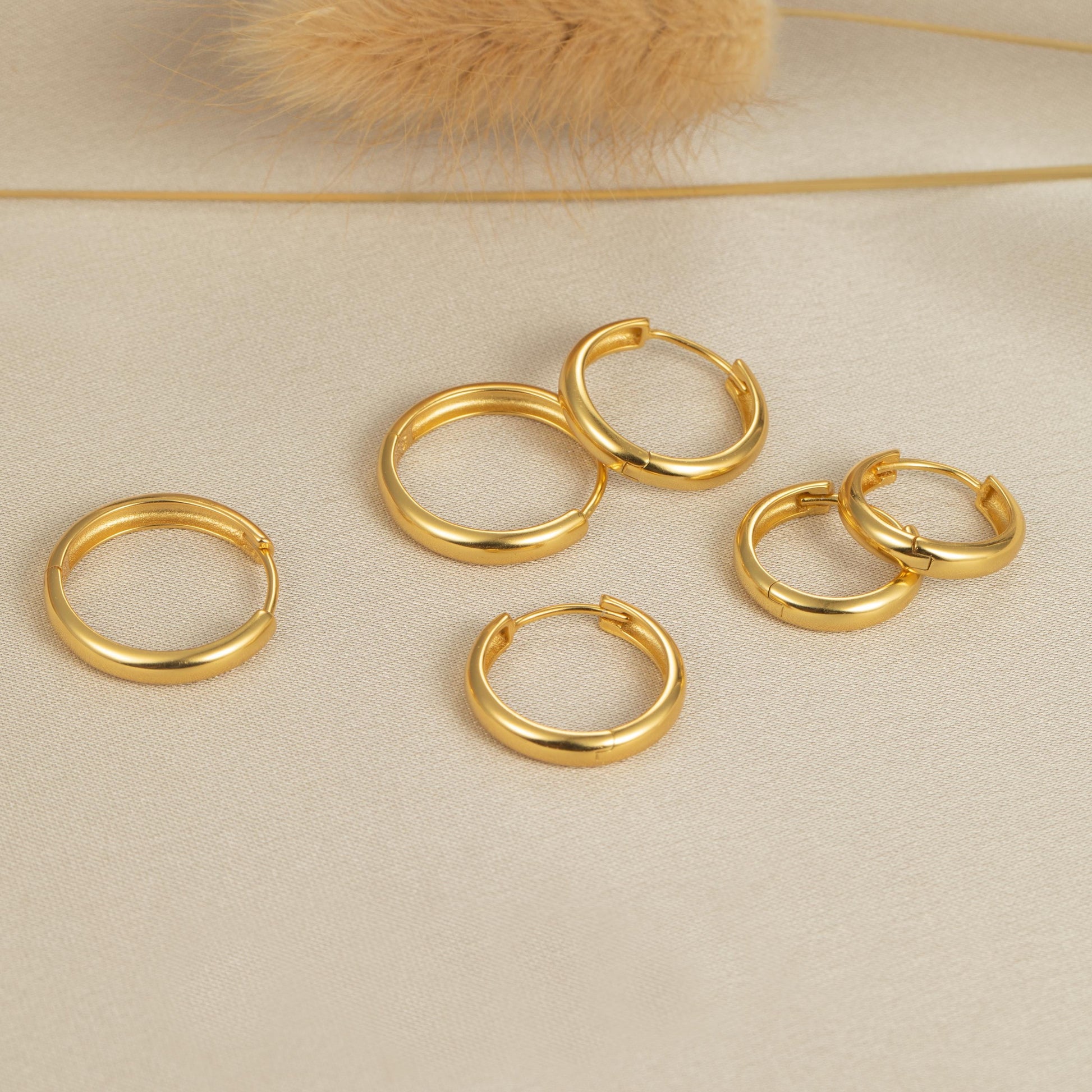 five pairs of gold hoop earrings on a white surface
